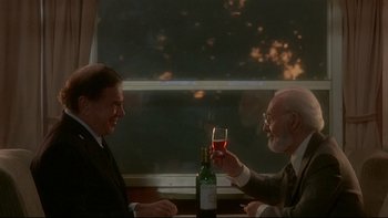 Movie still from “The Cassandra Crossing” (1976), directed by George P. Cosmatos – Two men sitting at a table with a glass of red wine; Medium shot, Over the shoulder angle