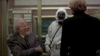 Movie still from “The Cassandra Crossing” (1976), directed by George P. Cosmatos – A man wearing a gas mask talking to two other people; Medium shot, Over the shoulder angle
