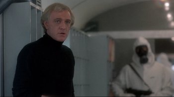 Movie still from “The Cassandra Crossing” (1976), directed by George P. Cosmatos – A man in a black shirt is standing in a room; Medium shot, Over the shoulder angle
