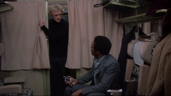 Movie still from “The Cassandra Crossing” (1976), directed by George P. Cosmatos – A man in a suit and a woman in a black dress; Medium shot, Over the shoulder angle