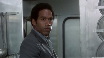 Movie still from “The Cassandra Crossing” (1976), directed by George P. Cosmatos – A man in a gray suit standing in front of a train; Close Up shot, Over the shoulder angle