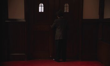 Movie still from “The Cathedral” (2021), directed by Ricky D'Ambrose – A man in a suit standing in front of an open door; Wide shot, High angle