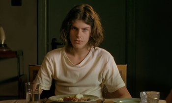Movie still from “The Cement Garden” (1993), directed by Andrew Birkin – A man sitting in front of a plate of food at a table; Close Up shot, Low angle