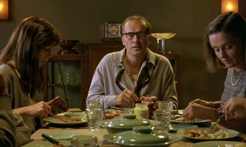 Movie still from “The Cement Garden” (1993), directed by Andrew Birkin – A man sitting at a dinner table eating pizza; Medium shot, Over the shoulder angle
