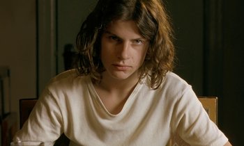 Movie still from “The Cement Garden” (1993), directed by Andrew Birkin – A man with long brown hair wearing a white t - shirt; Close Up shot, Low angle