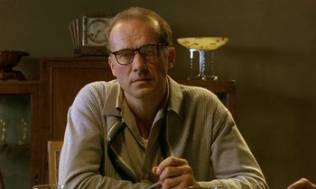 Movie still from “The Cement Garden” (1993), directed by Andrew Birkin – A man sitting in front of a table with a clock on the wall; Close Up shot, Low angle