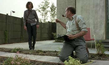 Movie still from “The Cement Garden” (1993), directed by Andrew Birkin – A man with a pipe in his mouth and another man with a pipe in his mouth; Medium shot, Low angle
