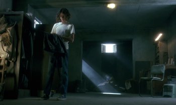 Movie still from “The Cement Garden” (1993), directed by Andrew Birkin – A person standing in a room with a book; Wide shot, Low angle