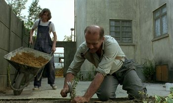 Movie still from “The Cement Garden” (1993), directed by Andrew Birkin – A man cutting a plant with a large knife; Wide shot, Low angle