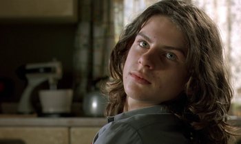 Movie still from “The Cement Garden” (1993), directed by Andrew Birkin – A young man with long hair and green eyes looking at the camera; Close Up shot, Low angle