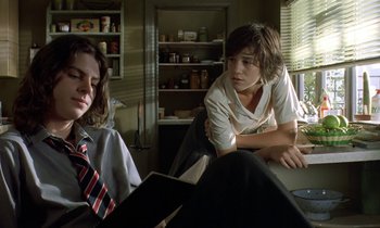 Movie still from “The Cement Garden” (1993), directed by Andrew Birkin – Two people sitting at a table in a room; Medium shot, Low angle