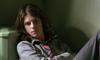 Movie still from “The Cement Garden” (1993), directed by Andrew Birkin – A man with long hair wearing a shirt and a tie; Close Up shot, Low angle