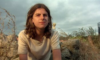 Movie still from “The Cement Garden” (1993), directed by Andrew Birkin – A man with long hair sitting on top of a hill; Close Up shot, Low angle