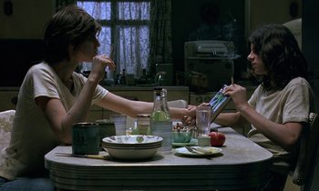 Movie still from “The Cement Garden” (1993), directed by Andrew Birkin – Two people sitting at a table with food and drinks; Medium shot, High angle