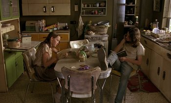 Movie still from “The Cement Garden” (1993), directed by Andrew Birkin – Two people sitting at a table in a kitchen; Wide shot, High angle