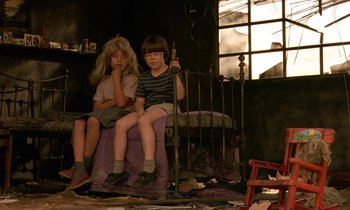 Movie still from “The Cement Garden” (1993), directed by Andrew Birkin – Two young children sitting on a chair in a room; Medium shot, High angle