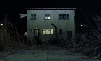 Movie still from “The Cement Garden” (1993), directed by Andrew Birkin – An abandoned building with a window lit up at night; Extreme Wide shot, Low angle