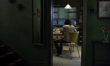 Movie still from “The Cement Garden” (1993), directed by Andrew Birkin – A person sitting at a table in front of a mirror; Wide shot, High angle