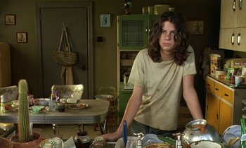 Movie still from “The Cement Garden” (1993), directed by Andrew Birkin – A woman sitting at a table with food on it; Medium shot, Low angle