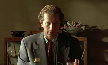 Movie still from “The Cement Garden” (1993), directed by Andrew Birkin – A man wearing a suit and tie sitting at a table; Close Up shot, Low angle