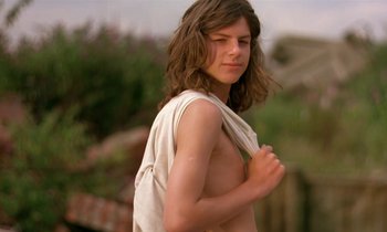 Movie still from “The Cement Garden” (1993), directed by Andrew Birkin – A young man with long hair and a white shirt is posing for a picture; Medium shot, Low angle