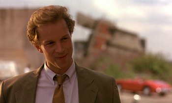 Movie still from “The Cement Garden” (1993), directed by Andrew Birkin – A man wearing a suit and tie standing in front of a building; Close Up shot, Low angle