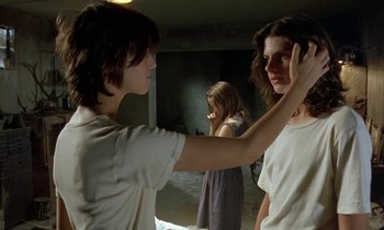 Movie still from “The Cement Garden” (1993), directed by Andrew Birkin – Two women and a man in a dark room; Medium shot, Over the shoulder angle