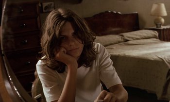 Movie still from “The Cement Garden” (1993), directed by Andrew Birkin – A woman sitting in front of a bed in a room; Close Up shot, High angle