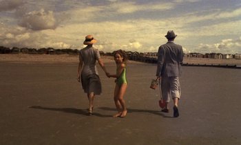 Movie still from “The Cement Garden” (1993), directed by Andrew Birkin – A little girl is holding hands with a man and a woman; Wide shot, High angle