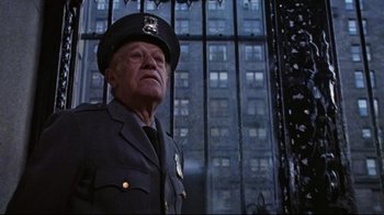 Movie still from “The Changeling” (1980), directed by Peter Medak – An older man in a police uniform stands in front of a building; Medium shot, Low angle
