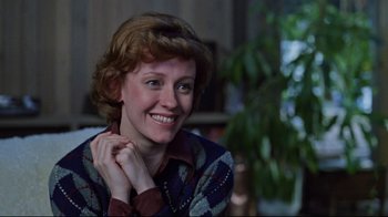 Movie still from “The Changeling” (1980), directed by Peter Medak – A woman smiles while sitting in front of a green plant; Close Up shot, Over the shoulder angle