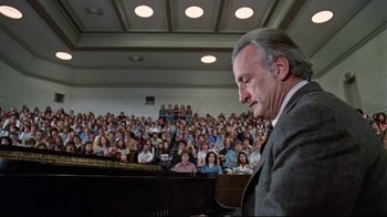 Movie still from “The Changeling” (1980), directed by Peter Medak – An older man sitting in front of an audience; Wide shot, High angle