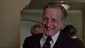Movie still from “The Changeling” (1980), directed by Peter Medak – A man in a suit and tie smiling for the camera; Close Up shot, Over the shoulder angle