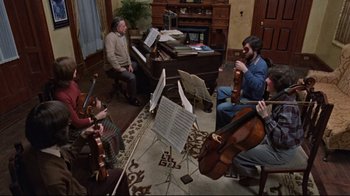 Movie still from “The Changeling” (1980), directed by Peter Medak – A group of people sitting in a living room playing musical instruments; Wide shot, High angle