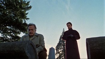 Movie still from “The Changeling” (1980), directed by Peter Medak – A man and a woman standing next to each other in front of trees; Wide shot, Low angle