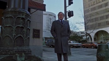 Movie still from “The Changeling” (1980), directed by Peter Medak – A man in a gray coat standing on the side of the street; Wide shot, Low angle