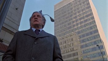 Movie still from “The Changeling” (1980), directed by Peter Medak – An older man in a suit and tie standing in front of a tall building; Medium shot, Low angle