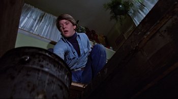 Movie still from “The Changeling” (1980), directed by Peter Medak – A man in a blue shirt and blue pants is crouching down; Medium shot, Low angle