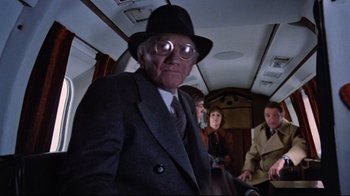 Movie still from “The Changeling” (1980), directed by Peter Medak – An old man wearing a hat and glasses; Medium shot, Over the shoulder angle