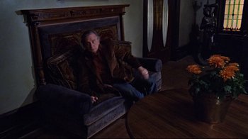 Movie still from “The Changeling” (1980), directed by Peter Medak – A man sitting on top of a couch in a living room; Wide shot, High angle