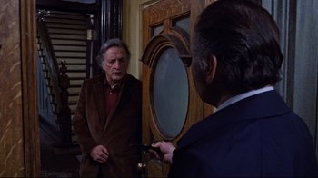 Movie still from “The Changeling” (1980), directed by Peter Medak – A man in a brown jacket is talking to another man in a blue suit; Medium shot, Over the shoulder angle
