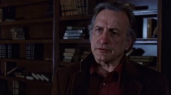 Movie still from “The Changeling” (1980), directed by Peter Medak – An older man in a red shirt and a brown jacket in front of a book shelf; Close Up shot, Low angle