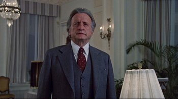Movie still from “The Changeling” (1980), directed by Peter Medak – An older man wearing a suit and tie in front of a lamp; Medium shot, Low angle