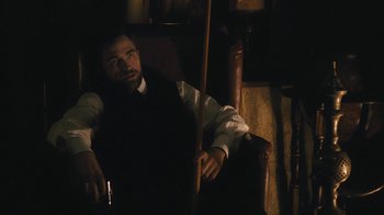 Movie still from “The Childhood of a Leader” (2015), directed by Brady Corbet – A man sitting in a leather chair in a dark room; Medium shot, High angle