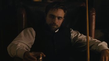 Movie still from “The Childhood of a Leader” (2015), directed by Brady Corbet – A man sitting in a chair holding a cigarette in his hand; Medium shot, Over the shoulder angle