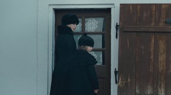 Movie still from “The Childhood of a Leader” (2015), directed by Brady Corbet – A woman and a child are standing in front of a door; Medium shot, Over the shoulder angle