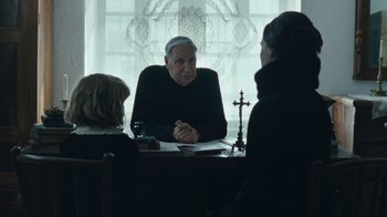 Movie still from “The Childhood of a Leader” (2015), directed by Brady Corbet – Three people sitting at a table in front of a window; Medium shot, Over the shoulder angle