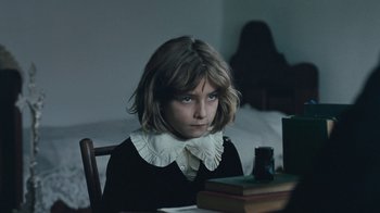 Movie still from “The Childhood of a Leader” (2015), directed by Brady Corbet – A young girl sitting at a table with a book; Close Up shot, Over the shoulder angle