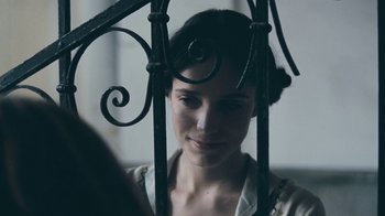 Movie still from “The Childhood of a Leader” (2015), directed by Brady Corbet – A woman looking through a wrought - iron gate; Close Up shot, Over the shoulder angle