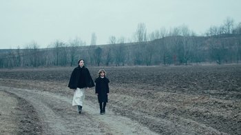Movie still from “The Childhood of a Leader” (2015), directed by Brady Corbet – Two people walking on a dirt road in a field; Wide shot, Low angle